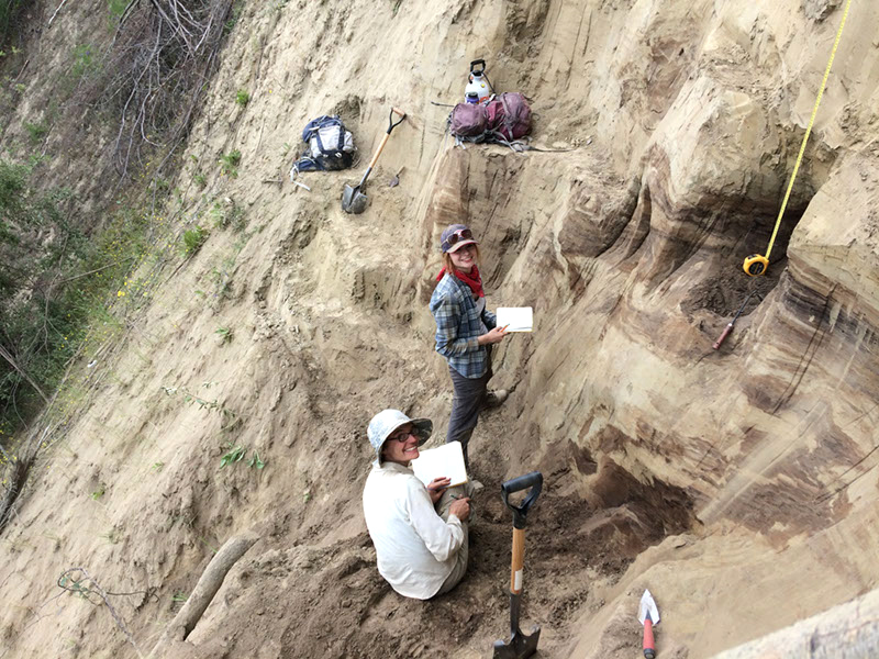 Elizabeth Thomas (left), University of Buffalo assistant professor of geology, and Kayla Hollister (right), UB geology master's student, take notes while perched on a wall of sediment. Credit: Britta Jensen