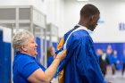 A student receives some help adjusting his robe during the College of Arts and Sciences afternoon commencement in Alumni Arena. 