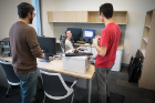 IT support specialist Mackenzie Lynch (seated) chats with graduate student Joe Costa (left) and user support specialist Spencer Miliotto while installing computer equipment.