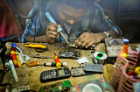 A repairer fixes the motherboard of a cellphone. Note the lack of safety equipment, such as gloves or a mask.