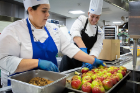Amelia Ruiz (blue apron), assistant executive chef, and Chef Manager Karen Long get to work prepping apples for baking.