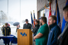 Dan Ryan (at podium), director of veteran services, speaks while student-veterans stand next to their branch flags: (from left) Chanel Powell, Army; Michael Powers, Marines; Justin Downey, Navy; Alexander Nowasell, Air Force; Andrew Cook, Coast Guard; Taylor Ashmore, POW/MIA (out of frame).
