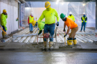 Workers use a flat edge to screed the surface and smooth it out.