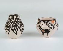 Two clay vessels were made by the artist Lucy Lewis. On the left, the pot is a creamy white clay with a black jagged pattern, and on the right, the pot is the same color as with some tan accents and a deer figure is the central design point. 