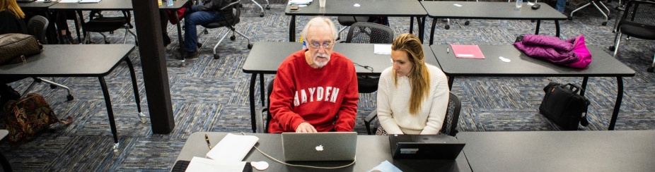 Faculty member using a computer while receiving course support from a learning designer. 