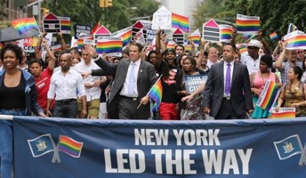 Governor Andrew Cuomo marching in a LGBTQ parade with a banner saying New York Led The Way. 