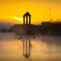 Three Grecian pillars monument from a distance shot over the lake at dusk with geese flying in the distance. 
