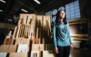 Photo shows a woman in a blue shirt standing in front of an architectural model. 
