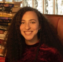 Smiling woman in a red shirt next to a stack of books. 