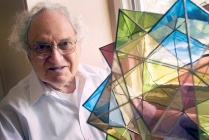 man in glasses with a mane of white hair, with a crysta-llike structure crafted from multi-colored glass. 