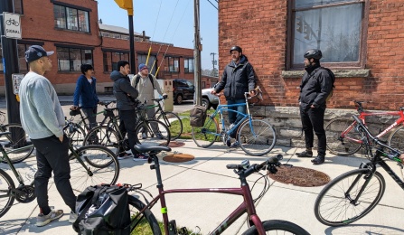 Several people stand around a sidewalk with bikes. 
