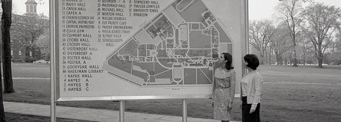 Two women standing beside a large map of the university. 