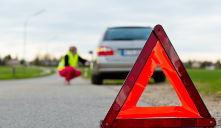roadside assistance caution triangle in a roadway with car off to side in background. 