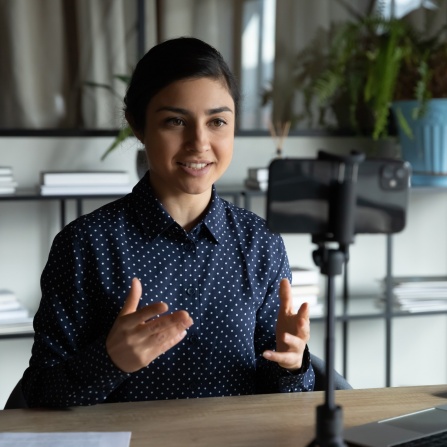 Royalty-free stock photo ID: 1694217805 Smiling indian ethnic girl sitting in front of smartphone on stabilizer, recording self-presentation video or sharing professional skills. Happy young smart businesswoman filming educational lecture. 