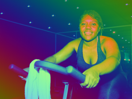 students posing on a stationary bike smiling at the camera with a glowing rainbow color effect overlay. 