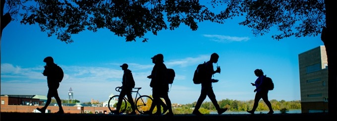 students walking on campus, silhouetted against a blue sky. 