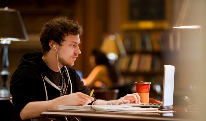 A student studying in the library with coffee and earbuds. 
