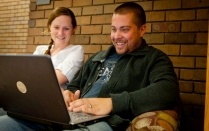 Two students smile and view a laptop screen. 