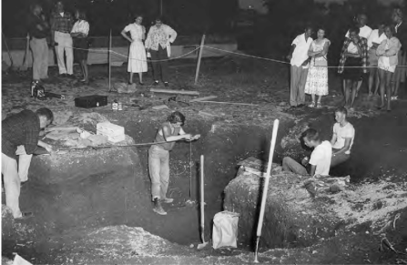 A black and white photo of Marian E. White (center) at an archeological dig at night. 