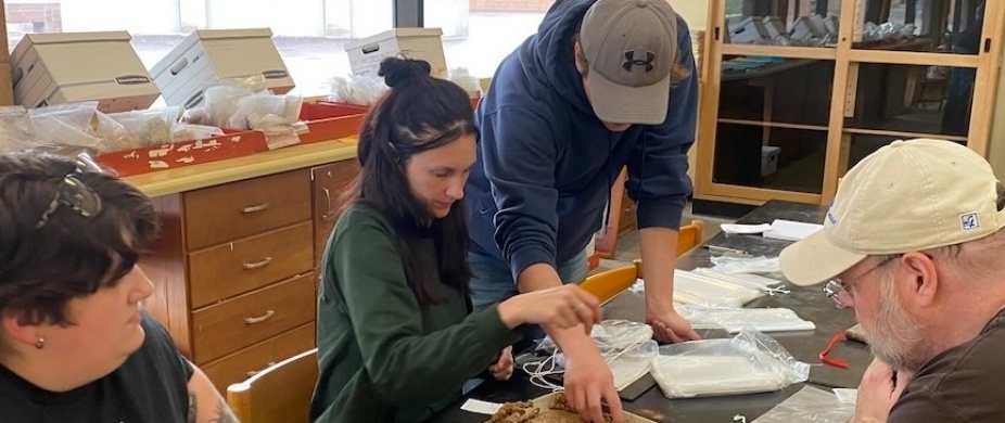 Students and faculty member at a large table working with archeological specimens. 