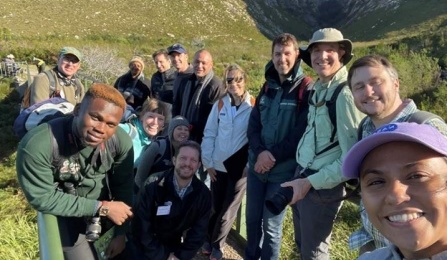 A group of people wearing hiking grear pose together in a green, moutainous area. 