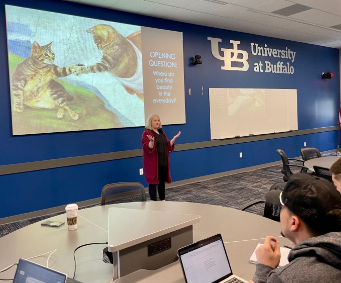 Sarah Vincent, associate teaching professor of philosophy, stands in a classroom with a slide behind her that asks, "Where do you find beauty in the everyday?".