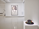 An installation photo of Thinking in Indian at UB Anderson Gallery. Here we see two works, in the foreground a beaded hat by Samantha Jacobs, and in the background a giant drawing of a figure with hair standing straight up, and something inside the hair by Shelly Niro called "Indian Brains.". 