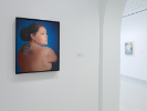 An installation photo from UB Anderson Gallery. In the foreground on a wall we see a painting of a Native American woman with a tattooed, bare back. She is looking over her shoulder, almost towards us but not quite. 