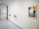 In another installation photo of UB Anderson Gallery, the closes work we can make out is a framed piece on the wall where in a circle in the middle a figure stands. Surrounding him in each corner are more figures. 