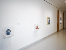 An installation photograph from UB Anderson Gallery exhibition Thinking in Indian. Two vitrines are on the wall, in the closer more legible one we see a ceramic vesel, blue and white. It looks like it has waves and fish carved or painted on it. 