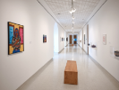 This installation photograph of UB Anderson Gallerys exhibition Thinking In Indian shows the second floor hallway. In the foreground we see one painting of an indigenous male figure casually leaning against a yellow background. 