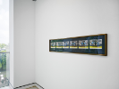 An installation photo from UB Anderson Gallery at a wide angle. There is one long framed photograph in the foreground but the contents are not clear or legible. 