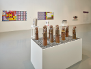 An installation photo of Thinking in Indian at UB CFA Gallery. In the foreground is a work where 11 ceramic figures and rocks stand atop a large pedestal table. The work is called "Prophesy Works" by Pete Jones. 