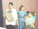 Dental Assisting school student holds plaque while woman and children look on