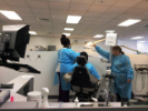 Dental Assisting school student working on another student seated in dental chair while faculty member directs them