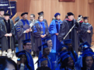 Audience, graduates and faculty stand at attention