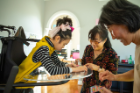 Yuna (left) plays with colorful stickers. Her mother, Soo-Kyung Lee (center, in glasses), and one of her caregivers, Haesu Little, keep her company. Credit: Douglas Levere / University at Buffalo