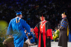 A graduate shakes the hand of President Satish K. Tripathi. At right is College of Arts and Sciences Dean Robin Schulze.