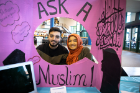 Mohammad Khan (left) and Sujana Chowdhury stand behind a colorful "Ask a Muslim!" sign during the World Bazaar in the Student Union lobby.
