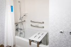 A large tub with a shower bench and several handrails in the bathroom of the accessible room.