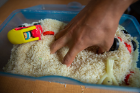 To help with their fine motor skills, children can pick up objects from the middle of a container of a material like rice, perhaps choosing by color or shape to connect with their classroom learning. They can also immerse their hands completely to feel the weight of the material on their hands.