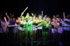Excited students covered in green glow paint throwing their UB horns up at the GloZone Paint Party! 