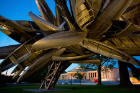 Large abstract structure made out of boats sits in the foreground with a view of the Albright Knox Art Gallery behind it. 