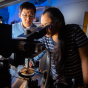 Two people in a lab using a microscope. 