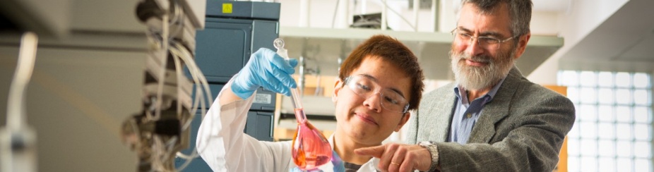 Professor and student in a lab holding a vial with red liquid. 