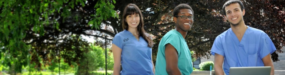 Three UB students in scrubs sit outside with a laptop. 