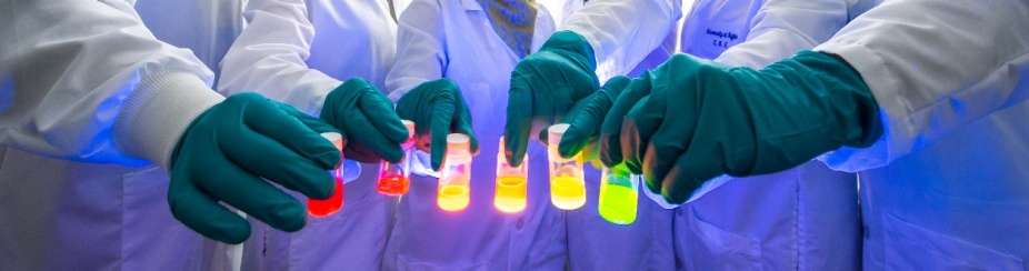 Gloved hands hold vials of glowing liquid in a range of colors. 