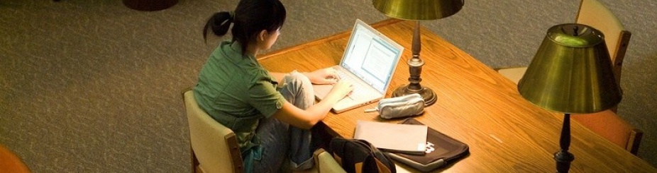 Student working on a laptop sitting at a desk with a lamp. 