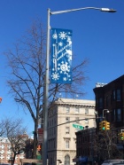 A blue banner with white snowflakes on it hanging on a street light. 