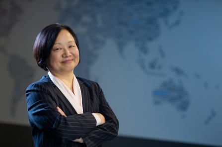 Wooksoo Kim standing, arms crossed, in front of an image of the globe. 